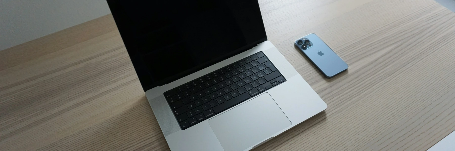 Laptop und Handy auf einem hellen Holztisch, ohne Personen